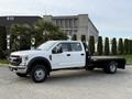A white 2020 Ford F-550 truck with a flatbed configuration parked with a crew cab and black wheels