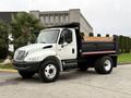A white 2006 International 4200 dump truck with a black bed and striped tailgate parked on a solid surface