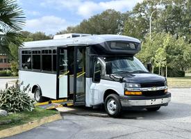 A 2020 Chevrolet Express bus with a black front and white body featuring an open door and a ramp for accessibility