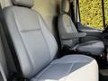 Two gray leather seats in the front of a 2015 Ford Transit van with armrests and a clean interior design