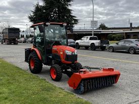 A 2018 Kubota B2650 tractor with a front-mounted broom attachment parked on the side of the road