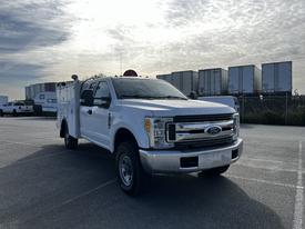 A white 2017 Ford F-350 SD truck with a service body and a red light on top parked in a lot