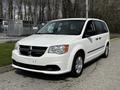 A white 2011 Dodge Grand Caravan with a sleek design and front grille featuring the Dodge emblem parked on a paved area