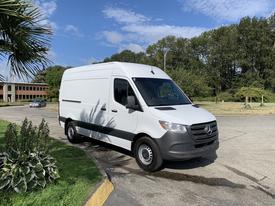 A white 2021 Mercedes-Benz Sprinter van with a high roof and rear cargo doors parked on the side of a road