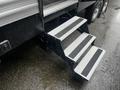 Three-step outdoor staircase with black frame and white textured steps leading up to an RV