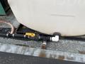 A close-up of a plumbing connection on a 2011 Hightliner Aquacide Hot Water Weed Control Dual Flat Deck Trailer featuring a large tank and several hoses with valves and fittings