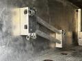 A metallic loading ramp with two support arms and secured hooks mounted on a wall inside a vehicle trailer