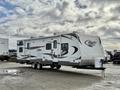 A white and tan 2013 Keystone Cougar travel trailer with a patterned design and a front hitch on display