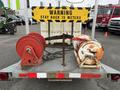 A dual flat deck trailer with two large orange and red hose reels mounted on the back and a yellow warning sign that reads STAY BACK 15 METERS