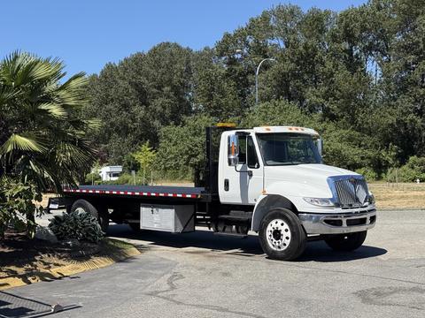 A 2018 International DuraStar flatbed truck with a white cab and black flatbed, featuring reflective striping and mounted lights on the roof