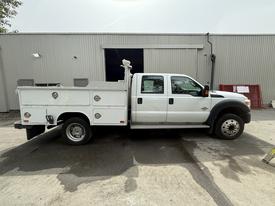A 2011 Ford F-450 SD truck with a white body and metal utility bed featuring multiple compartments and tools mounted on the side
