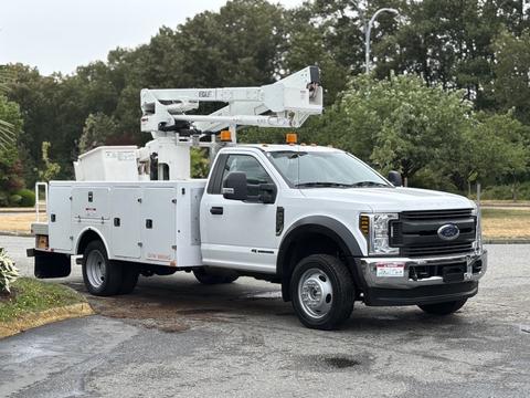 A white 2018 Ford F-550 truck with a bucket lift mounted on the bed and a service box on the side, designed for utility work and equipped with safety lights