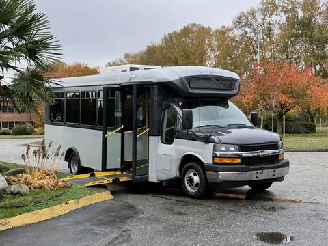 A 2019 Chevrolet Express bus with a wheelchair ramp lowered and doors open, parked with its front facing the viewer