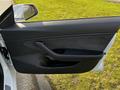 The interior door panel of a 2019 Tesla Model 3 featuring a sleek design with a handle and speaker grille in a modern aesthetic