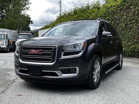 A gray 2016 GMC Acadia with a chrome grille and prominent GMC logo parked with its headlights on
