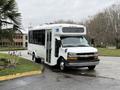 A 2013 Chevrolet Express shuttle bus with a wide side door open, featuring a white body and visible handicap accessibility signage on the exterior