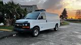 A 2005 Chevrolet Express van with a white exterior and black accents parked on a street with visible reflections on the wet pavement