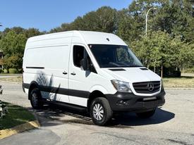A 2017 Mercedes-Benz Sprinter van in white with a black trim parked on a street featuring a high roof and large cargo space
