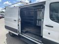 A 2019 Ford Transit van with the back doors open showing an empty cargo area with a black floor and metal shelving system on the sides