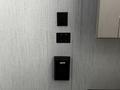Three black wall switches and a control panel mounted on a textured light gray wall