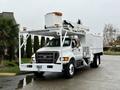 A white 2015 Ford F750 utility truck equipped with a large elevated platform and various tools on the side
