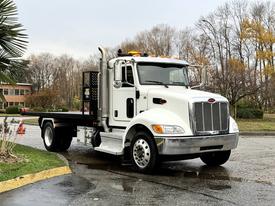 A 2020 Peterbilt 330 flatbed truck with a white exterior silver grille and orange roof lights parked on a wet surface