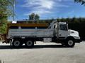 A 2005 Volvo VND 122 dump truck with a white cab and yellow dump bed, featuring a large rear pivot and dual rear wheels