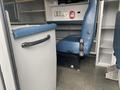 A blue driver's seat in a 2014 Chevrolet Express with a gray trash bin beside it and a small empty shelf in the background