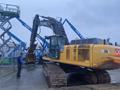 A 2014 John Deere 350G excavator with a large digging arm and tracks standing on a wet surface with a worker nearby