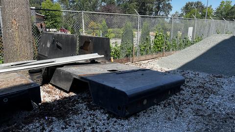 A 2000 Service Flat Deck lying on gravel with various metal parts and a partially visible plywood board nearby