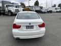 A 2011 BMW 3-Series parked with a white exterior and dual exhaust pipes visible at the rear