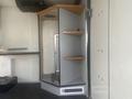 A 2004 Ford Econoline interior featuring a grey cabinet with wooden shelves and a small door, designed for utility or storage purposes