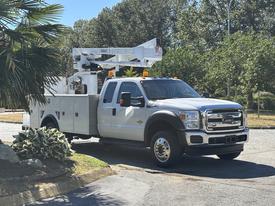 White 2016 Ford F-550 with a bucket lift attachment and utility bed parked on a street