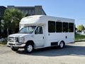A white 2016 Ford Econoline bus with large windows and a wheelchair lift on the side parked at an angle