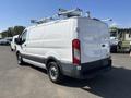 A white 2016 Ford Transit van with a high roof and roof rack, viewed from the rear and side, showcasing its cargo capacity and design