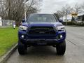 A 2022 Toyota Tacoma in a vibrant blue color features a bold front grille and large tires positioned directly facing the viewer