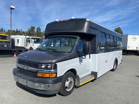 A 2017 Chevrolet Express bus with a gray front and white body featuring large windows and a step at the entrance