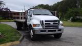 A white 2008 Ford F-750 flatbed truck with a chrome grille and multiple lights mounted on the roof