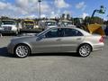 A 2007 Mercedes-Benz E-Class sedan in a metallic tan color with five-spoke alloy wheels parked at an industrial site