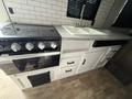 A compact kitchen featuring a black four-burner gas stove and a double sink with sleek white cabinetry and a gray countertop