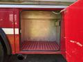 A compartment of a red fire truck with a metal interior and a grid floor, designed for storage, is shown with the door open
