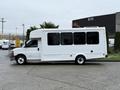 A side view of a 2015 Chevrolet Express shuttle bus with a white exterior and large windows parked on a concrete surface