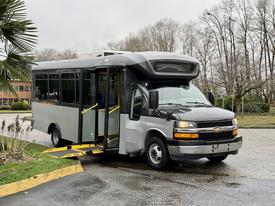 A 2020 Chevrolet Express bus with an extended entrance ramp and large windows is parked with its doors open, showcasing accessibility features.