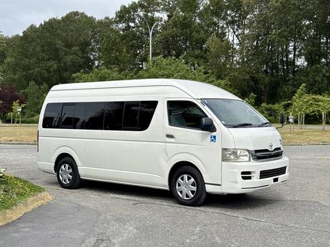 A white 2009 Toyota Hiace van with a high roof and large side windows parked in the foreground