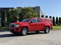 A red 2018 GMC Canyon pickup truck with a matching truck cap parked on a paved surface with greenery nearby