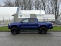 A blue 2022 Toyota Tacoma pickup truck with a crew cab and off-road tires parked on a paved surface