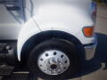 A white 2005 Ford F-750 truck with a shiny chrome wheel and tire focused on the front fender and wheel assembly