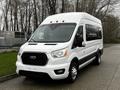 A 2021 Ford Transit van in white with a black grille and multiple windows parked on a paved surface