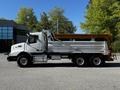 A white 2005 Volvo VND 122 dump truck with a silver and orange dump bed and large tires parked on a gravel surface