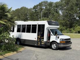 A white 2020 Chevrolet Express bus with large windows and yellow steps is parked, showcasing its spacious interior and modern design